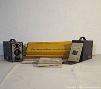 Overview photo showing two Brownie Target Six-20 cameras, Kodak movie light box, assorted film canisters, and manuals arranged on a cloth background.