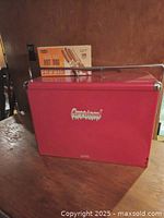 Red Carricool metal cooler with zinc lining and carry handle shown on a wooden surface.