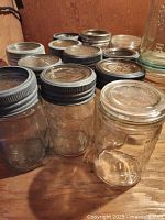 Twelve vintage Crown canning jars in various sizes displayed on wooden surface, showing metal screw caps and typical embossed designs.