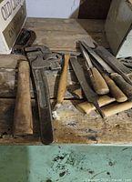 Photo showing wood files with wooden handles, an adjustable pipe wrench, and a wooden mallet on a worn wooden surface