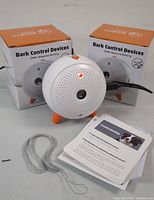 Photo showing two bark control devices with orange legs, instruction manuals, and wrist strap.