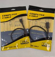 Front view of two sealed packages each containing a computer cable labeled 'COMPUTER CABLE' with packaging showing 'HIGH SPEED CABLE' and '100% Tested & Certified'. Each cable visible through packaging shows USB connectors.
