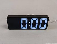 Front view of the black digital LED clock displaying 0:00 in bright blue numbers on a rectangular body.
