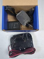 Photo of USB power adapter and black sensor device with red and black wires inside a box.