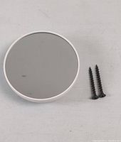 Front view of Google Nest Thermostat showing circular reflective surface with white perimeter and two mounting screws.