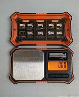 Top view of the digital jewelry weighing scale with open lid showing instruction printed inside and calibration weight placed beside the display.