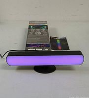 Photo showing the Monster Illuminessence Color Flow Light Bar illuminated in purple, displayed with its original box and instruction manual.