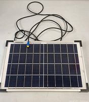 Front view of the rectangular solar panel with cable and blue connector on white surface.