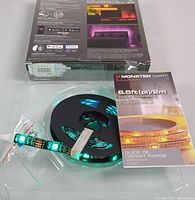 Photo showing the LED strip on spool lit in turquoise inside plastic packaging with quick start guide and box.