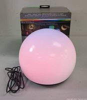Front view of the spherical white RGBW LED orb light powered by a black cord, with product box in rear