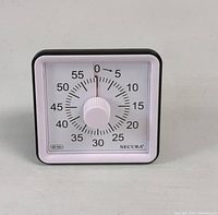 Square Secura mechanical timer with white dial and black frame. 60-minute countdown markings with a central manual knob.