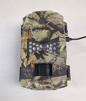 Front view of camouflaged Wosoda trail camera showing lens, infrared LEDs, and motion sensor.