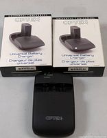 Two Optex Universal Battery Charger boxes and one charger unit in black with Optex branding