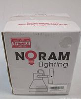 Outer packaging box of Noram Lighting wall sconce light fixture with branding and fragile handling warning.