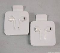 Photo shows two pairs of white wired earphones designed for iPhone displayed on white packaging cards on a plain surface.