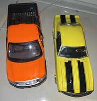 Top view of an orange 2010 Ford F-150 DTX die cast pickup truck with black bed and yellow 1968 Chevrolet Camaro die cast car with black racing stripes side by side