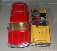 Top-down view of two toy cars placed side by side, showing the yellow convertible with the surfboard on its hood and the red station wagon with a ribbed roof and yellow tinted windshield.