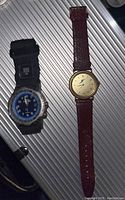 Photo showing two men's wristwatches on a metallic textured background, one Timex Indiglo with fabric strap and blue dial, the other a Japanese movement quartz with leather strap and gold-tone case.