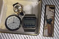Top view of three watch faces and decorative lighter on a white tray showing Timex mechanical, quartz face, and digital watch.