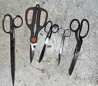 Photo showing five pairs of scissors of various sizes and types arranged side by side on a textured surface.
