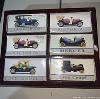 Photo showing six miniature model cars in their original labeled boxes inside a wooden display case. Boxes labeled Brougham, Victoria (two), Mercer, Ford Model T, and Town Coupé.