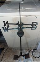 Top view of the antique weather vane showing the south and north directional markers and central rod.