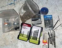 Overview of assorted drill bits, sets, loose bits, and bag of screws and nails on ground.