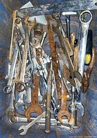 Top view of assorted wrenches in metal container showing various types including open-end, combination, and pipe wrenches.