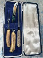 Carving fork, carving knife, and sharpening steel set with antler handles in blue velvet-lined case with cream satin lid interior.