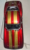 Top front view of the Maisto 1965 Chevrolet die cast model showing red body with gold dual racing stripes on hood and roof.