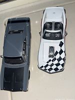 Top view of two 1/24 scale die cast cars: a grey 1969 Dodge Charger ST and a white 1970 Corvette with checkered racing decals.