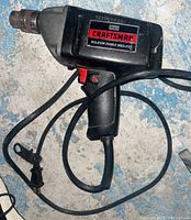 Full side view of the Sears Craftsman corded power drill showing its black body, red trigger, cord, and chuck.