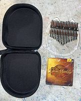 Photo of open padded black zippered case, 17-key kalimba with clear acrylic body, and Dean Markley vintage bronze acoustic guitar strings pack.