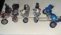 Five collectible toy motorcycles on display, showing four standing upright and one blue one lying on side.