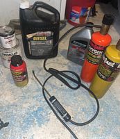 Overview photo showing large antifreeze container, red and yellow gas cylinders, small oil bottles, and hoses on blue floor surface.