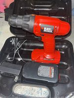 Red and black Black and Decker cordless power drill in black plastic carrying case with power supply and cord.