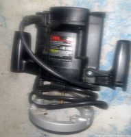 Side view of black SKIL plunge router showing motor housing, right side handle, and silver metal base with power cord coiled.