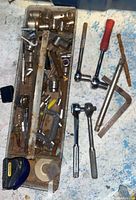 Photo showing a metal tray with assorted socket wrench handles, extensions, various sockets, a C-clamp, and measuring tape.
