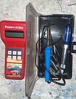 Photo of the Superchips Micro Tuner device alongside the soldering kit in a plastic case with tools and accessories.