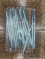 Close-up photo of several large hex head stud screws in a basket, showing the length and threading detail on the screws.