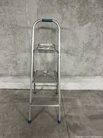 Front view of a silver 2-step aluminum ladder with a blue grip on the safety handle, ridged steps, and blue rubber feet caps.