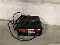 MotorMaster battery charger with cords visible on concrete ground against a wall.