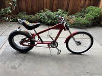 Side view showing red frame with flame graphics, padded banana seat with flame design, wide rear tire, chrome rear fender and rack.