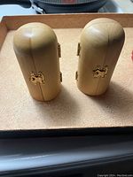 Two closed wooden triptych cases with rounded tops and brass hinges and clasps on a beige surface