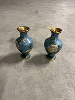 Pair of small cloisonné vases on concrete floor, blue with floral butterfly decoration and gold rims.