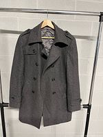 Front view of men's dark gray peacoat hanging on a rack showing double-breasted buttons, wide collar, epaulets, and cuff straps.