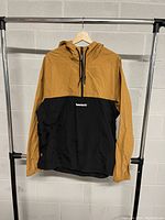Front view of the Timberland two-tone hooded coat hanging on rack, showing half-zipper, kangaroo pocket, and hood with drawstrings.