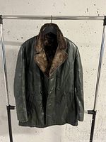 Front view of men's dark green leather coat with brown fur collar hanging on rack.