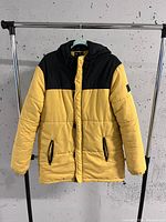 Front view of the yellow and black puffer coat hanging on a rack, showing front zipper and pockets.