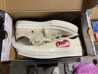 Profile view of new off-white Converse low-top sneaker inside box with red heart graphic on outer side.